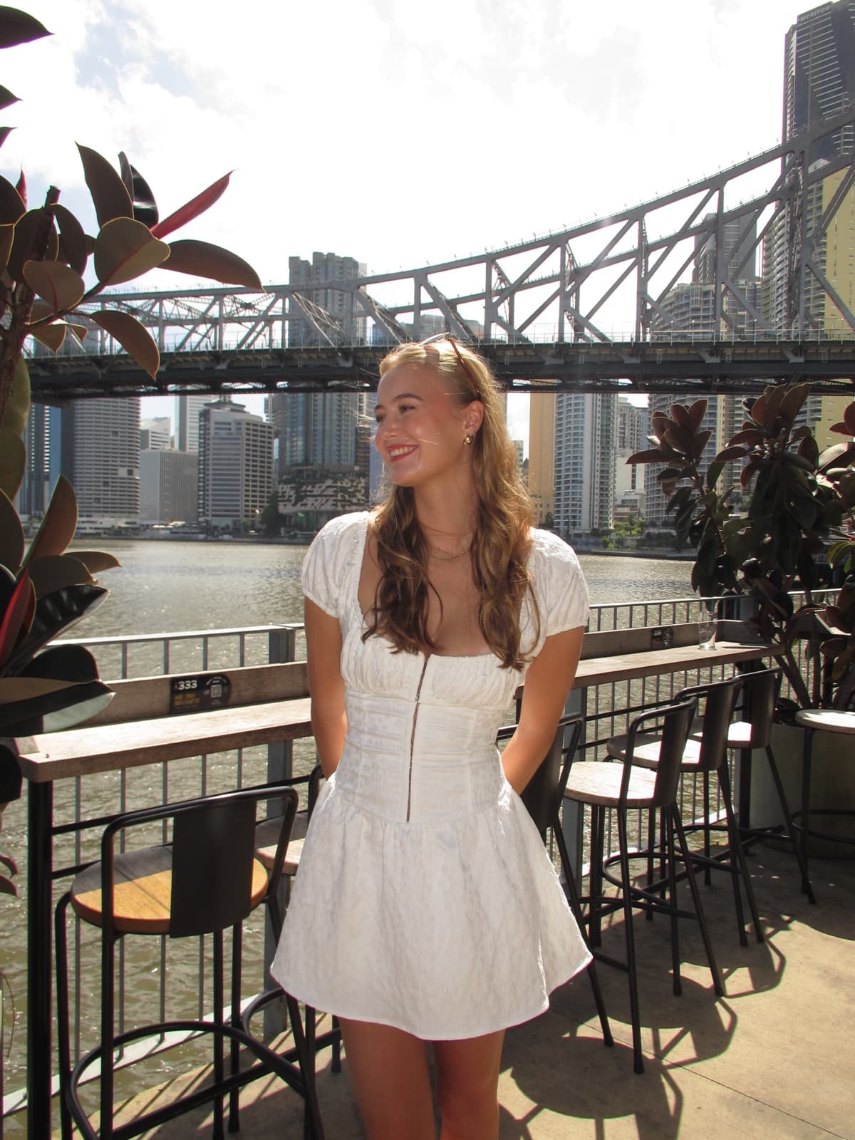 Hannah smiling in a white dress by the Brisbane river